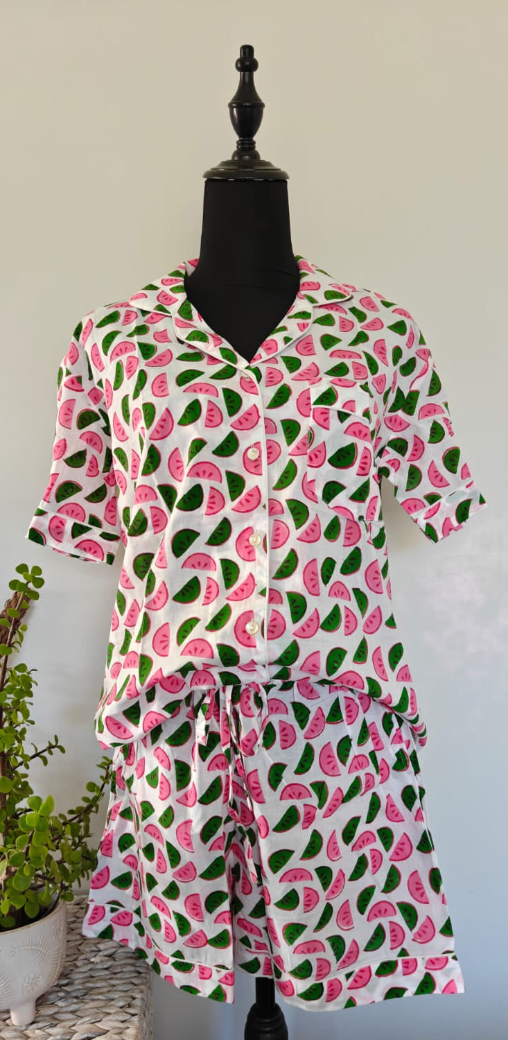 A short-sleeve button-front pyjama set with a tie waist, featuring a pink and green watermelon print on a white background, displayed on a black mannequin dress form.