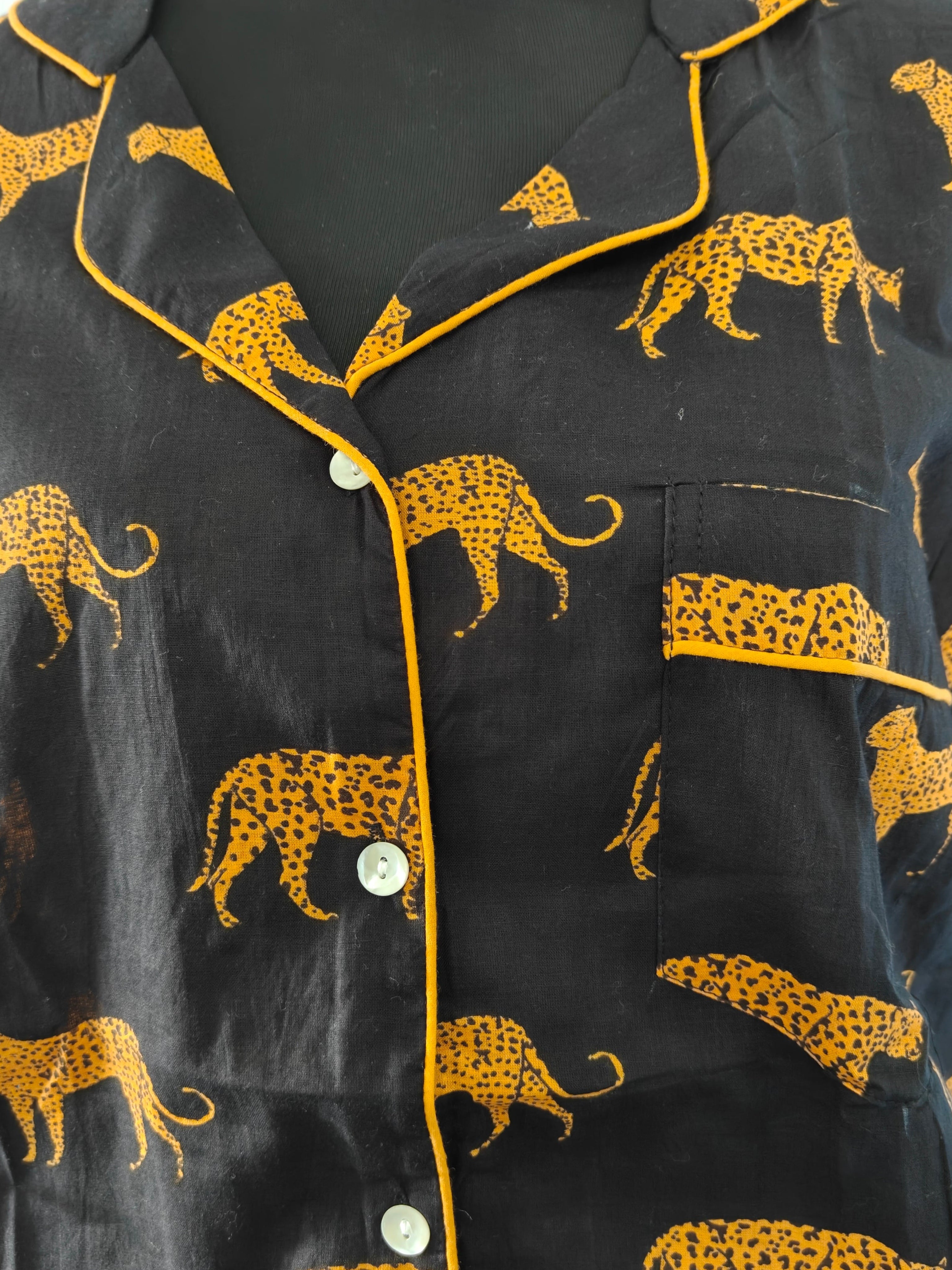Black short-sleeve pajama shirt with a yellow cheetah print and yellow piping trim, displayed on a black mannequin torso.