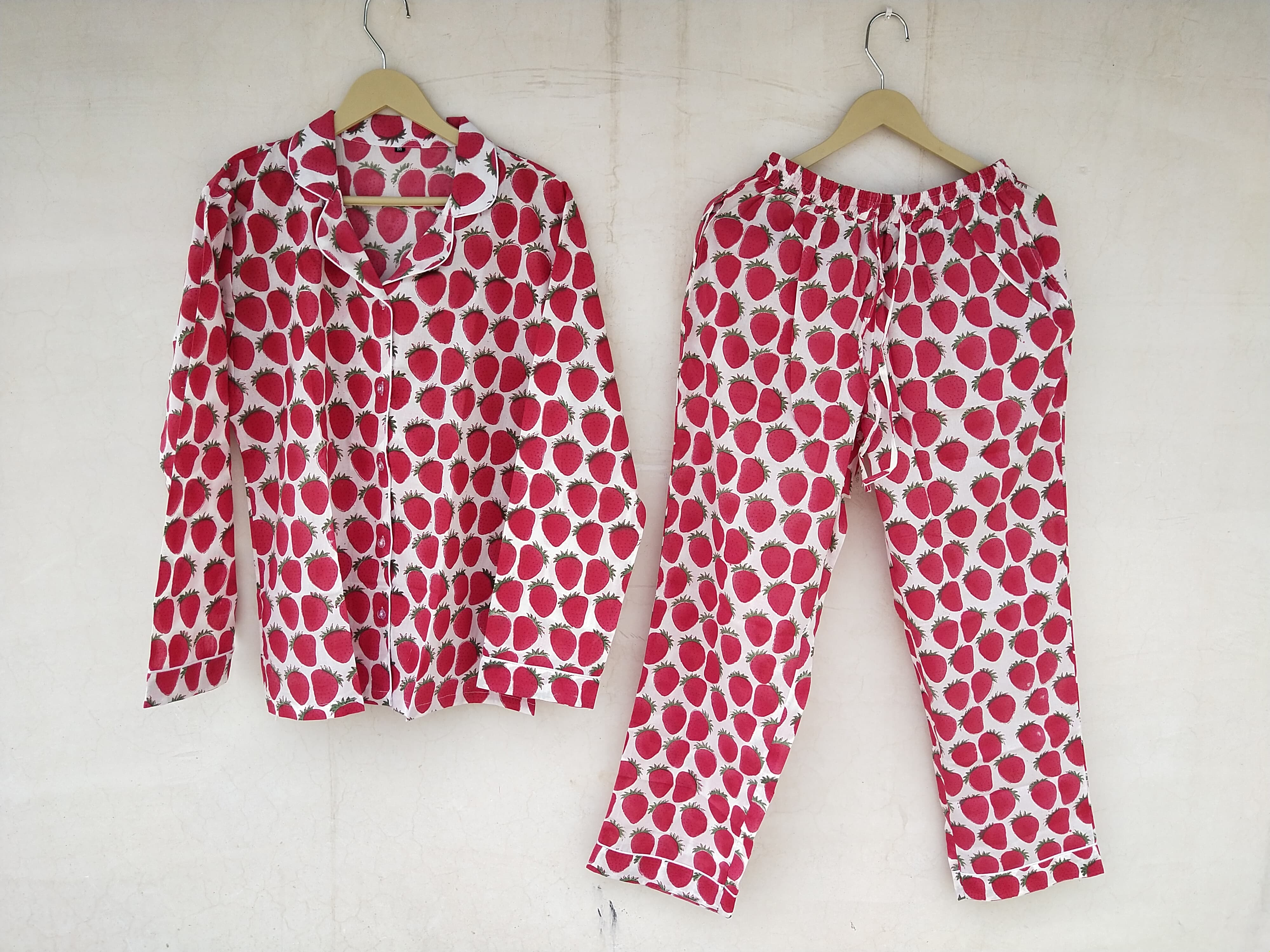 A pyjama set with a red strawberry pattern on a white background, displayed on hangers.