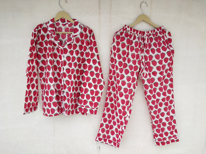 A pyjama set with a red strawberry pattern on a white background, displayed on hangers.